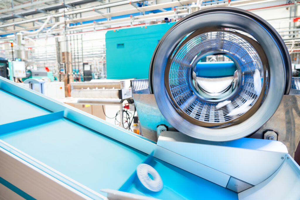 Ein Förderband mit einem rotierenden Zylinder in einer industriellen Umgebung, sichtbar sind mechanische Teile und Fördertechnik.