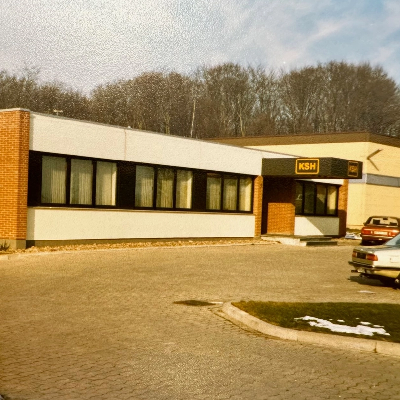 Historisches Gebäude der KSH GmbH aus den 1980er Jahren mit charakteristischer Fassade und Fenstern.