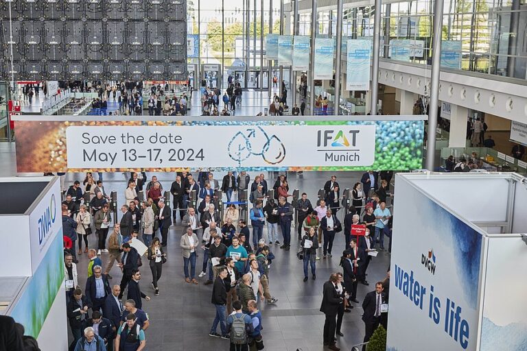 In einer gut besuchten Messehalle hängen Banner zur IFAT Munich 2024, daneben steht deutlich „Water is life“.